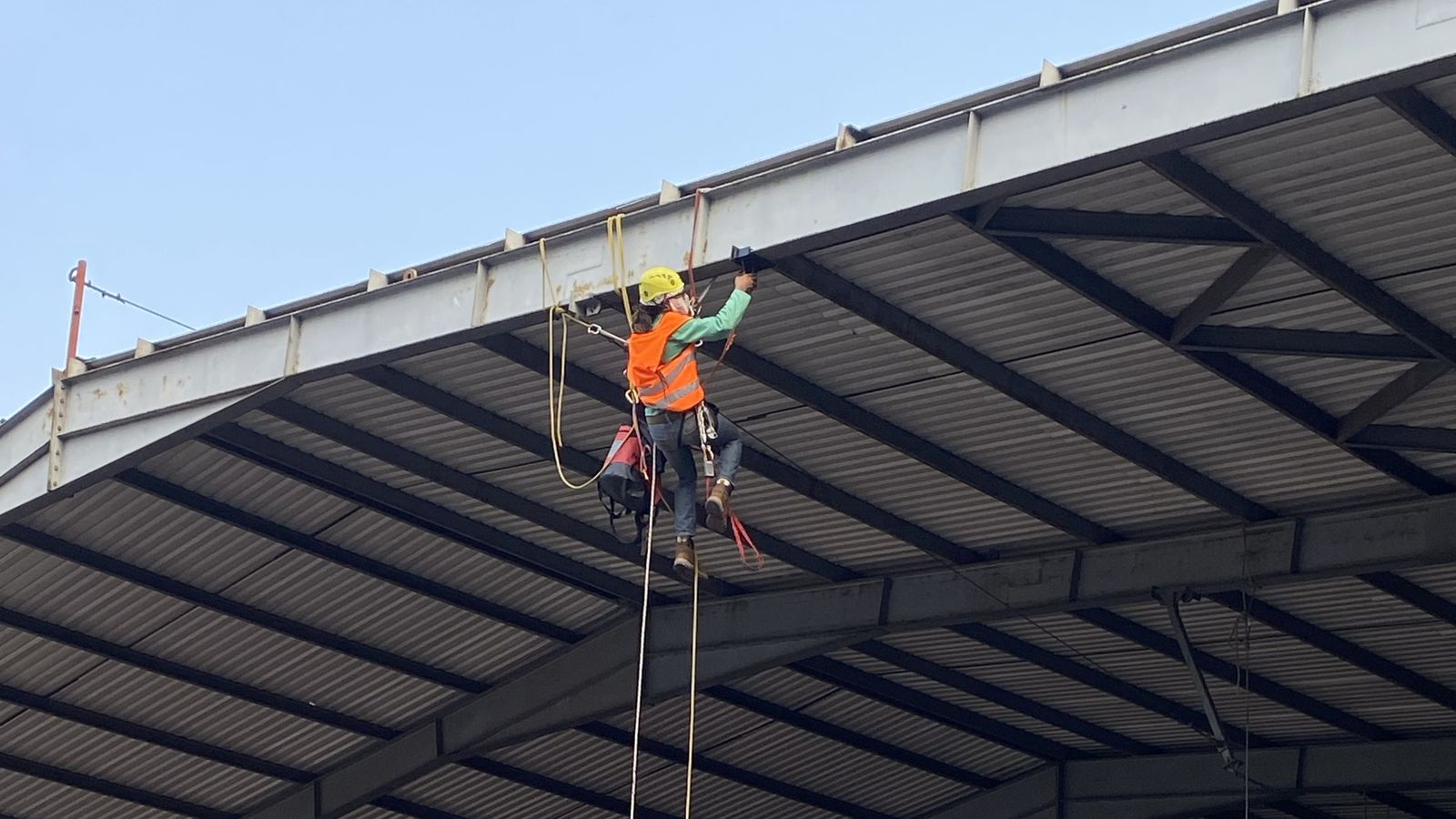 Técnico de Vertika con casco y arnés, suspendido bajo el techo de una nave industrial